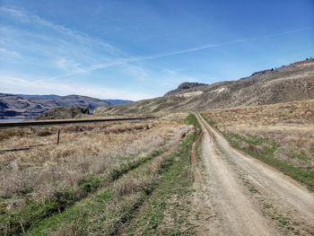 Dirt road amidst field against sky