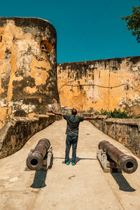 A man standing between two ancient canons at fort jesus - an ancient fortication in mombasa, kenya 