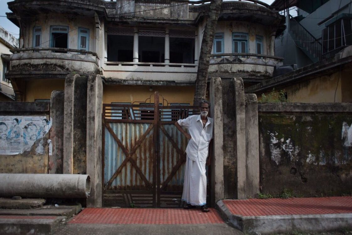REAR VIEW OF MAN STANDING BY WINDOW OF OLD ABANDONED HOUSE