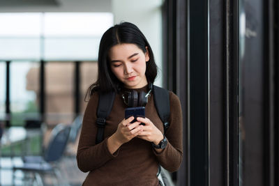 Young woman using phone while standing on mirror