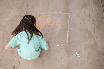 Girl draws with colorful crayons on pavement. children's drawings with chalk on wall. creative kid