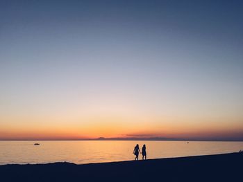 Rear view of silhouette friends walking at beach against sky during sunset