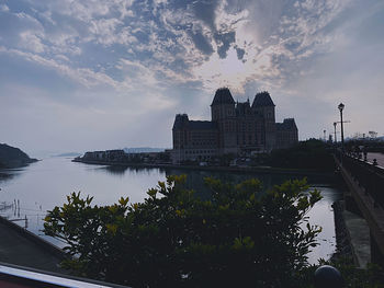 Buildings by river against sky at sunset