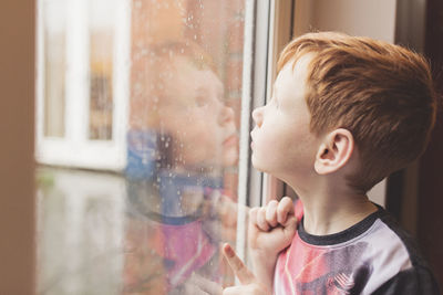 Boy looking at the rain on windowpane