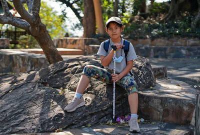 Full length of teenage boy sitting on rock