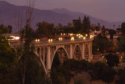 Bridge over illuminated city against sky at dusk