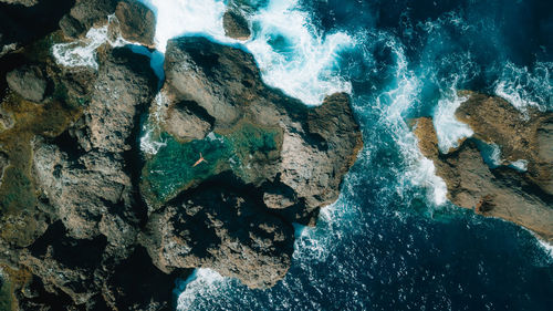 Aerial view of woman swimming in water amidst rock formation in sea