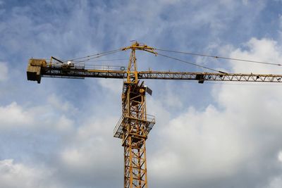 Low angle view of crane at construction site against sky