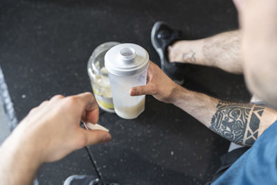 Close-up of sportsman holding protein shake while sitting in gym