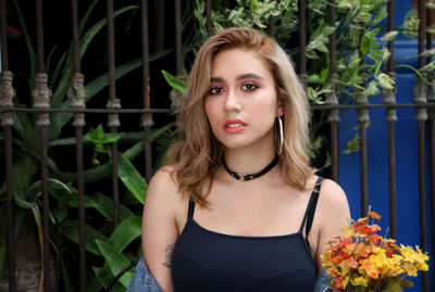 Portrait of beautiful young woman standing against fence