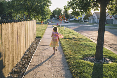 Rear view of girl wearing cape running on footpath during sunset