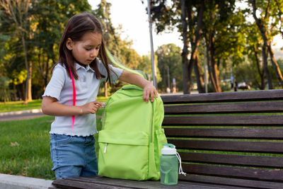 Young girl with backpack sitting on bench in park
