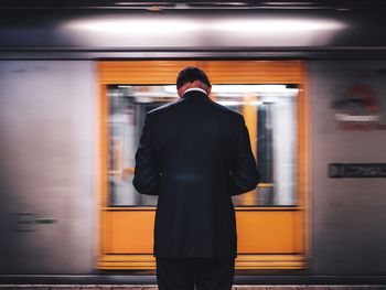 Rear view of man standing against moving train at station