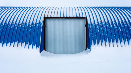 Snow covered metal fence against blue sky