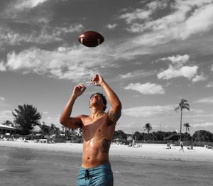 Man catching rugby ball while standing on shore at beach