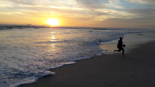 Girl playing at beach against sky during sunset