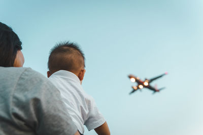 Rear view of man and airplane flying against clear sky