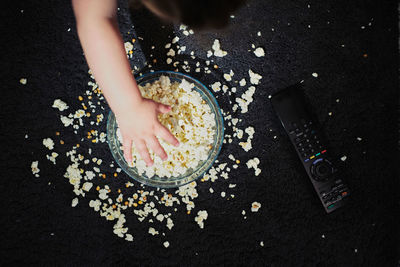 A bowl of popcorn on the floor with a small child's hand taking it fro