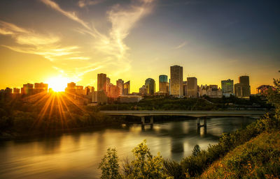 Scenic view of river by buildings against sky during sunset