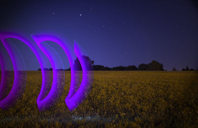 Digital composite image of illuminated field against sky at night