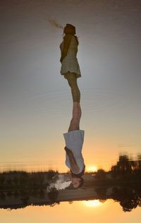 Woman standing on lake against sky during sunset