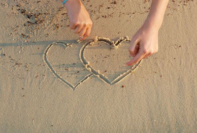 Midsection of hands holding heart shape on sand at beach