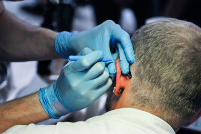 Close-up of artist piercing man ear at studio