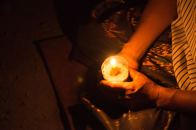 Midsection of woman holding illuminated candle while praying on floor