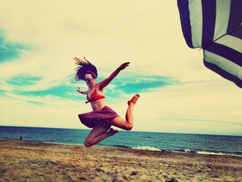 Full length of woman jumping at beach against sky