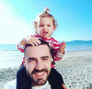 Portrait of happy father carrying daughter on shoulder at beach during sunny day