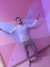 Full length portrait of woman standing against pink wall