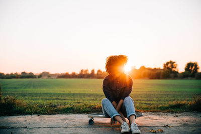 Full length of woman sitting on land against sky during sunset