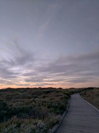 Boardwalk amidst field against sky during sunset