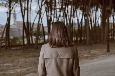 Rear view of woman wearing coat standing against trees on road