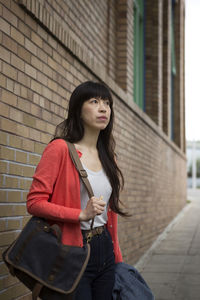 Young woman with shoulder bag standing on footpath by building