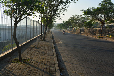 Man walking on footpath by road against sky in city