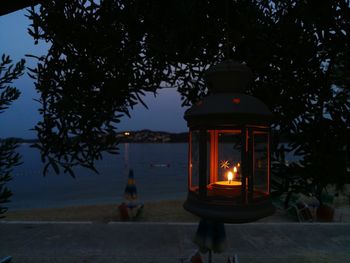Close-up of illuminated lantern on table against tree at night