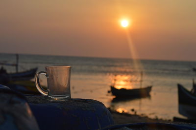 Drinking glass on sea against sky during sunset