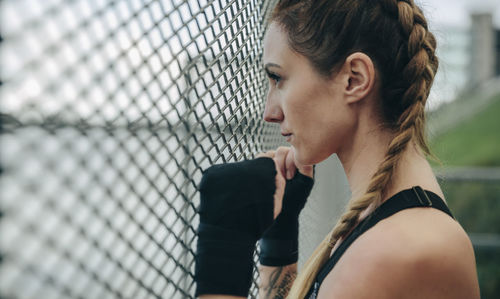 Woman looking away while standing by chainlink fence