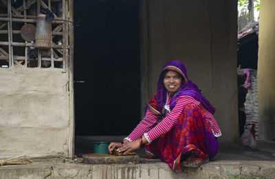 Portrait of woman sitting at entrance grinding spice in traditional way