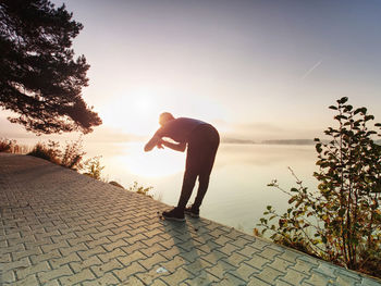 Side view of silhouette man standing on footpath at sunset