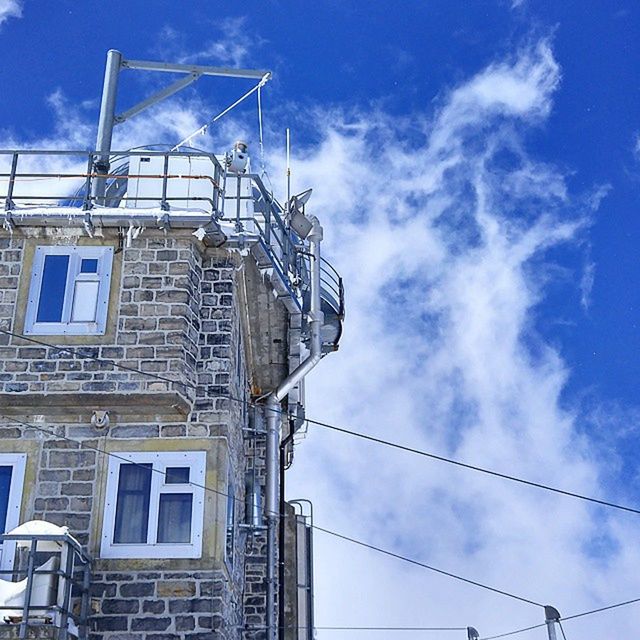 low angle view, sky, built structure, architecture, building exterior, blue, cloud - sky, cloud, power line, day, cable, outdoors, no people, building, sunlight, connection, electricity pylon, electricity, cloudy, power supply