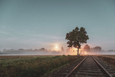 Railroad tracks amidst trees on field against sky