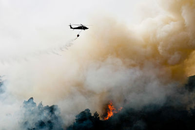 Silhouette helicopter extinguishing forest fire while flying over mountain