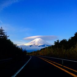 Empty road leading towards mt fuji against blue sky