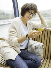 Smiling woman in eyeglasses texting on smartphone. millennials lifestyle. casual clothes.