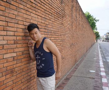 Portrait of man standing by brick wall on sidewalk