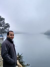 Portrait of young man standing in lake against sky