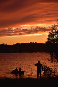 Silhouette people standing by lake against orange sky