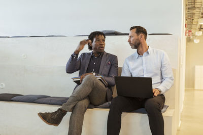 Serious businessman gesturing while talking to mature male colleague in office